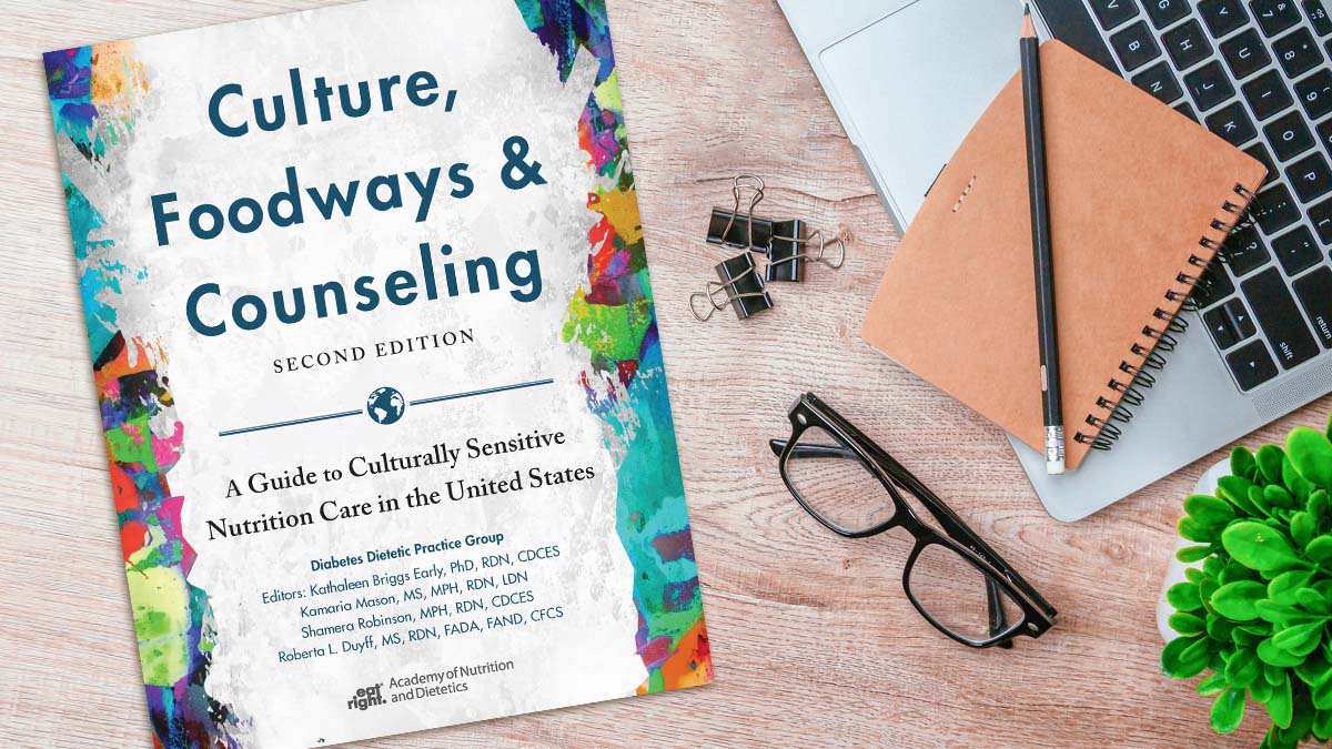 The book Culture, Foodways, and Counseling: A Guide to Culturally Sensitive Nutrition Care in the United States on a desk beside a laptop, notepad file clips and a pair of glasses